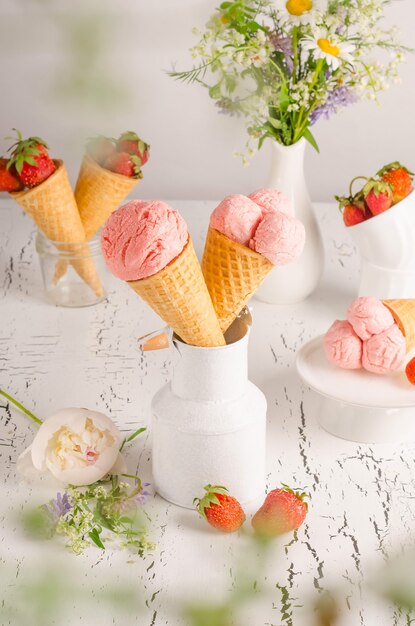 Strawberry ice cream in waffle cups on white wooden background