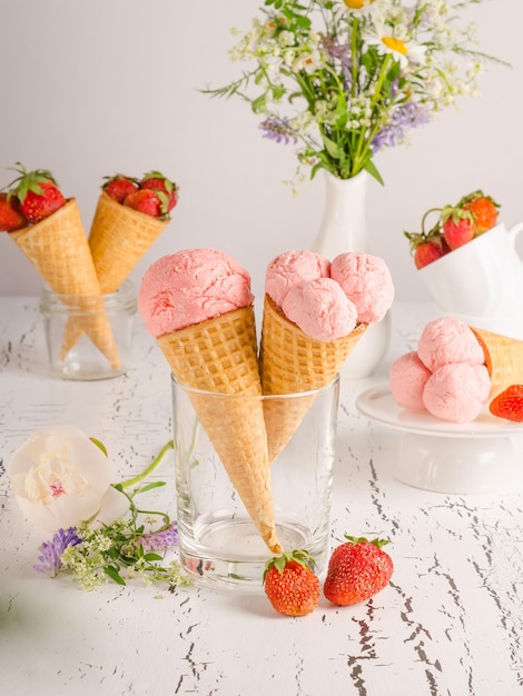 Strawberry ice cream with fresh strawberries in waffle cups on white wooden background