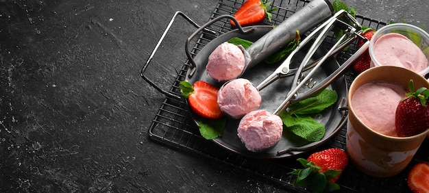 Strawberry ice cream with mint and strawberries Ice cream spoon On a black stone background top view