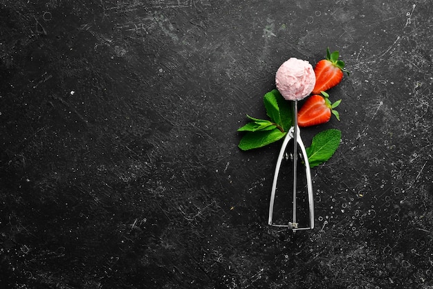 Strawberry ice cream with mint and strawberries Ice cream spoon On a black stone background top view