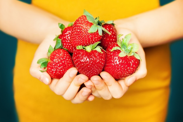 여성의 손에 딸기입니다. 노란색 바탕에 빨간 열매입니다. 건강한 식생활 개념