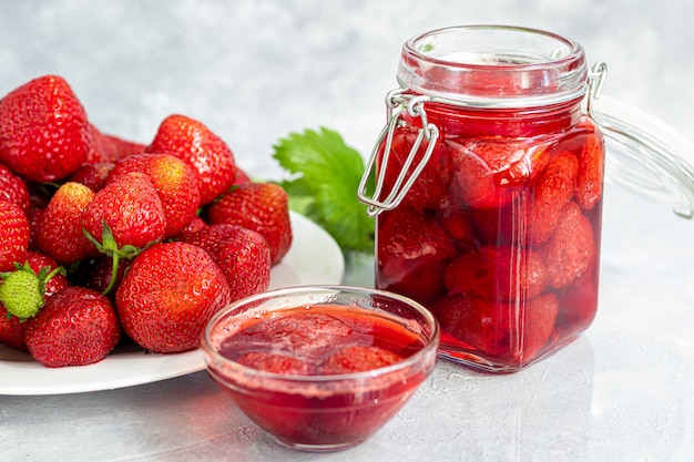 Strawberry jam in a glass jar next to fresh strawberries