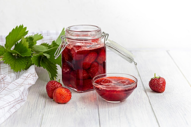 Strawberry jam in a glass jar next to fresh strawberries