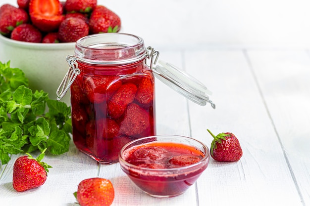 Strawberry jam in a glass jar next to fresh strawberries