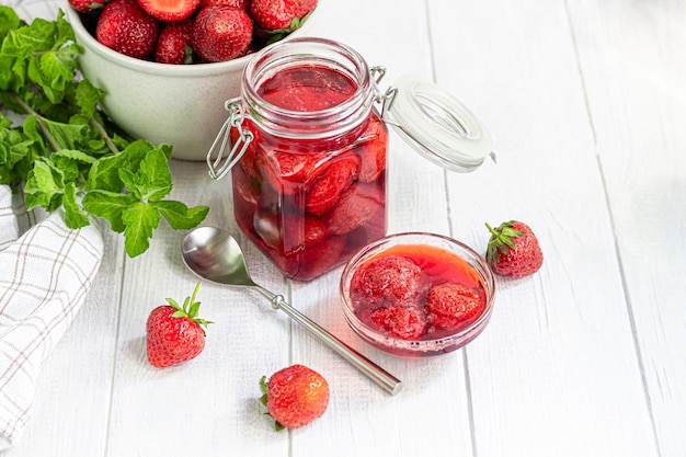 Strawberry jam in a glass jar next to fresh strawberries