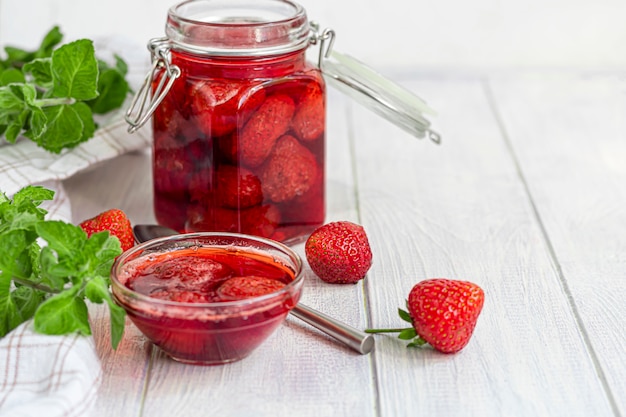 Strawberry jam in a glass jar next to fresh strawberries