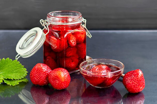 Strawberry jam in a glass jar next to fresh strawberries