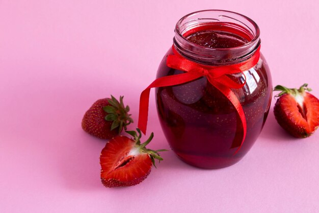 Strawberry jam in the glass jar on the pink background