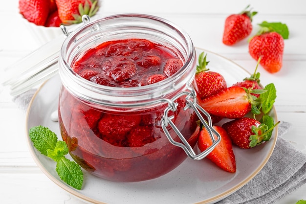 Strawberry jam in the glass jar with fresh berries on a white wooden table Summer dessert Copy space