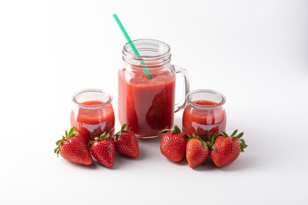 Strawberry juice in glass jug next to juicy strawberries isolated on white background