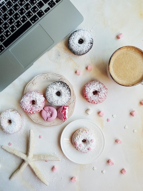 Ciambelle dolci di macarons alla fragola e lavanda con tazza di cappuccino e marshmallow su tavola di marmo