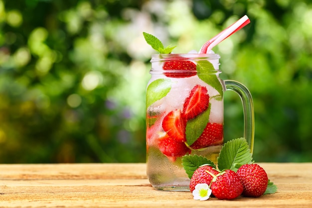 strawberry lemonade with ice and mint in mason jar on wooden table outdoor