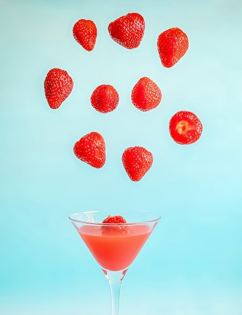 Strawberry levitation over a glass with strawberry nectar on a\
blue background the concept of a he