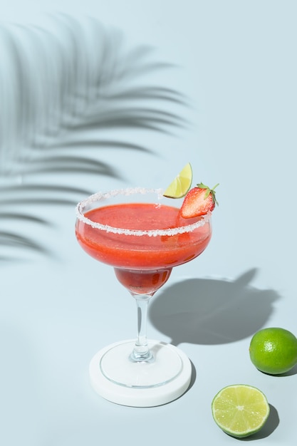 Strawberry margarita cocktail with lime and ice cube on blue background