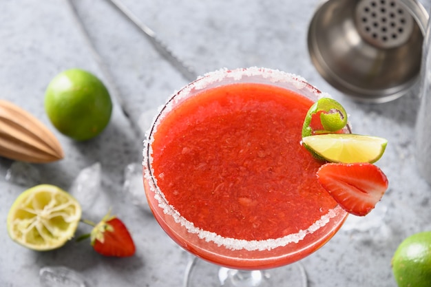 Strawberry margarita cocktail with lime juice and ice cube on black background vertical orientation