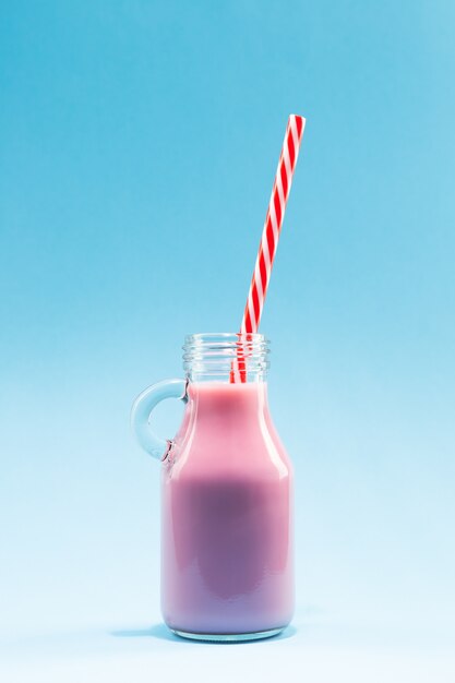 Strawberry Milk Shake Pitcher with Straw, on blue background.