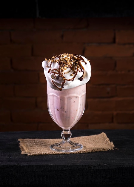 Strawberry milk shake with whipped cream chantily on black wood, with bricks on background