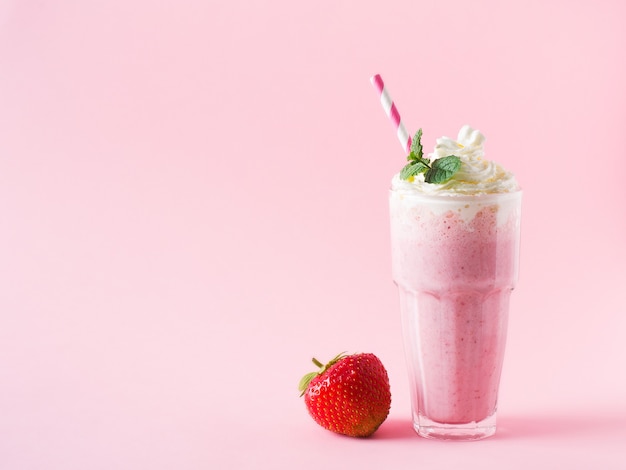 Strawberry milkshake or smoothie and fresh raw berries on pink