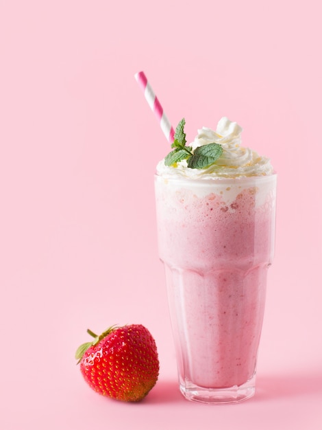 Клубничный молочный коктейль или смузи и свежие сырые ягоды на розовом