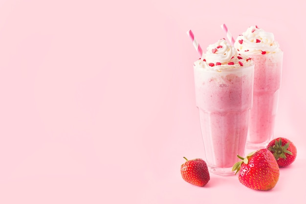 Strawberry milkshake or smoothie and fresh raw berries on pink