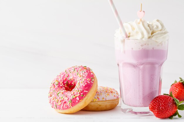 Strawberry milkshake with whipped cream and glazed donut on a white background