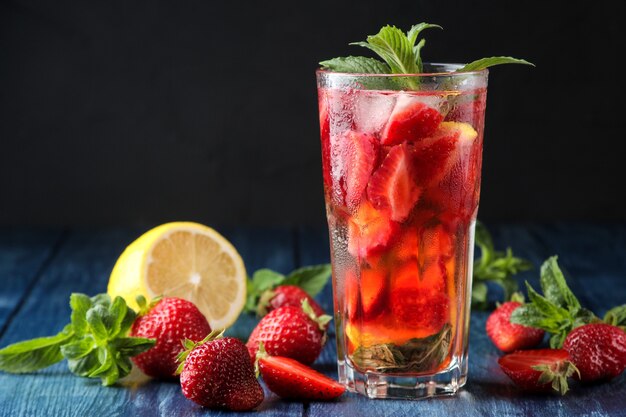 Strawberry Mojito. Cold summer mojito cocktail with strawberries, mint, lemon and ice in a glass on a blue wooden table. on a dark background