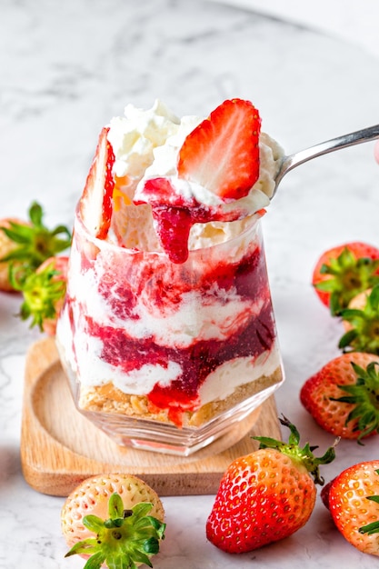 대리석 테이블 위에 놓인 유리잔에 담긴 딸기 무스 케이크 뚜렷한 층이 있는 딸기 무스 케이크는 얇게 썬 신선한 딸기로 아름답게 장식되어 있습니다.