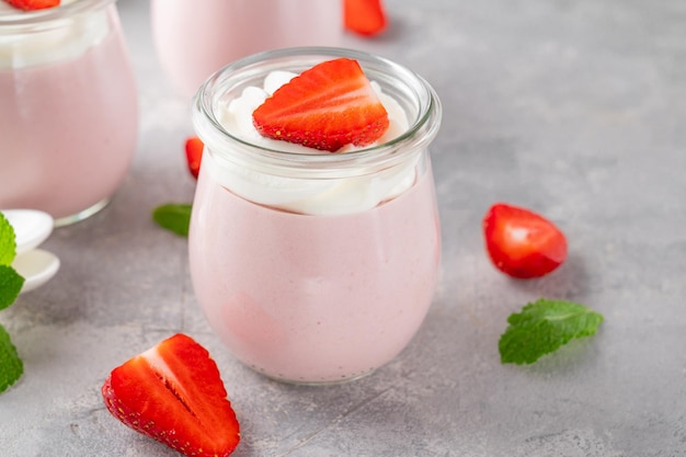 Strawberry mousse in a glass jar with whipped cream fresh berries and mint leaves, summer dessert