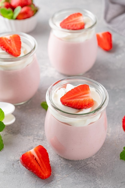 Strawberry mousse in a glass jar with whipped cream fresh berries and mint leaves Summer dessert