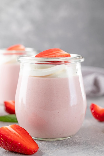 Mousse di fragole in vasetto di vetro con panna montata ai frutti di bosco freschi e foglie di menta