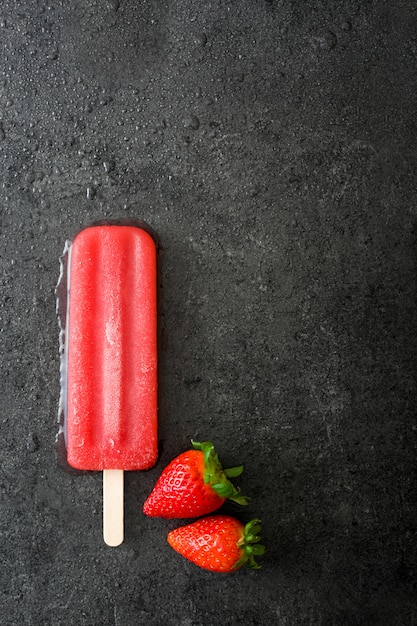 Strawberry popsicle on black stone top view copy space