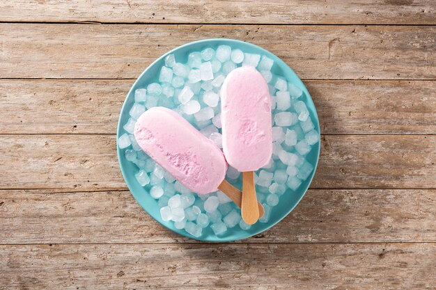 木製のテーブルの上の青いプレートにイチゴのアイスキャンディーと砕いた氷