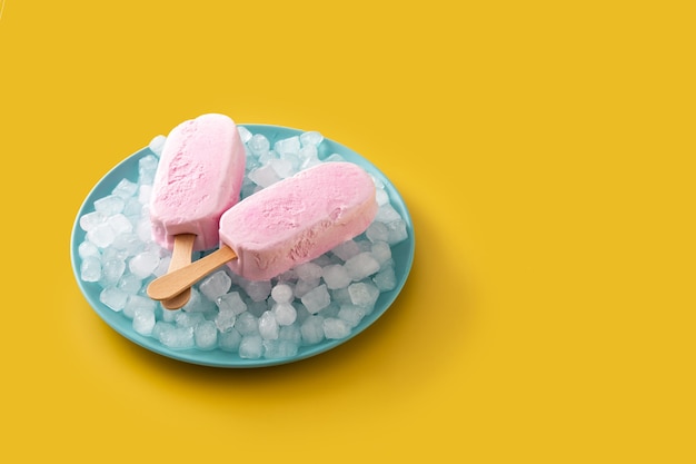 Strawberry popsicles and crushed ice on blue plate on yellow table