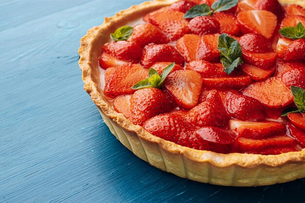 Strawberry quiche with lime zest and strawberry slices laid on top and topped with lime jelly on a blue wooden table