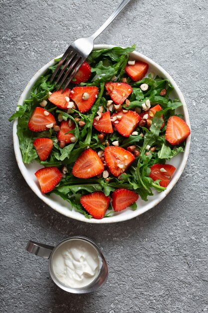 Strawberry salad with arugula on a plate with a fork on light grey background