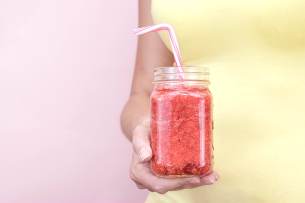 Strawberry smoothie in a glass close-up. Women's hand holds a drink