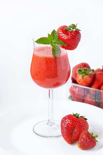 Strawberry smoothie in a glass on a high leg decorated with strawberries and mint.