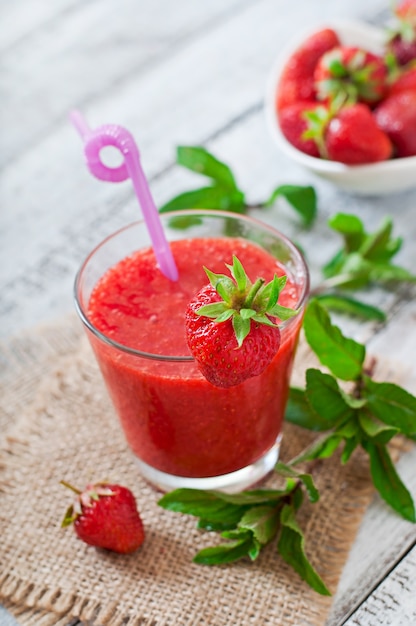 Strawberry smoothie in glass and mint leaves on a wooden surface in rustic style