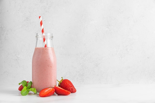 Photo strawberry smoothie or milkshake in a glass bottle with straw and mint on white background