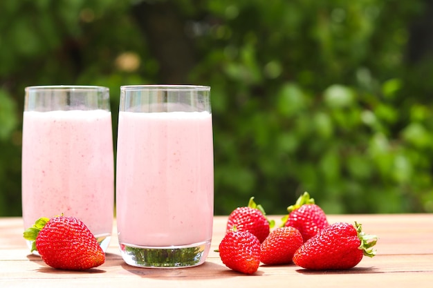 Strawberry smoothie or milkshake in two glasses against lush folliage Summer drinks outdoor