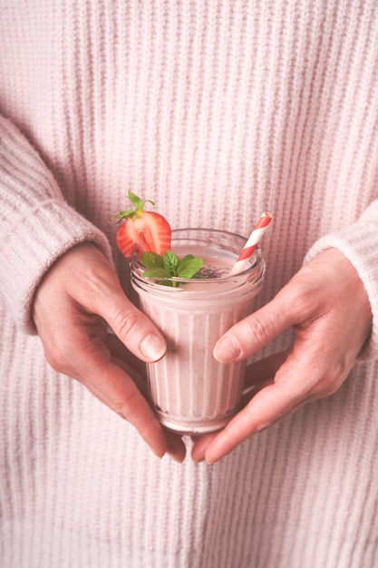 Strawberry smoothie Vegan smoothie from strawberry banana chia seeds and mint in glass in hands of female wearing pink sweater Clean eating alkaline diet weight loss food concept Mock up