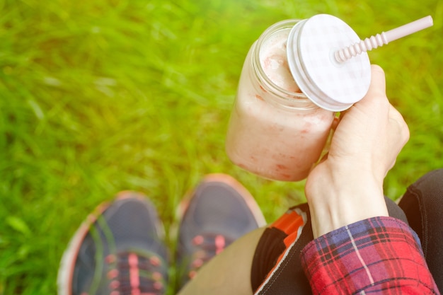 Strawberry smoothies in hand and sneakers on a surface of green grass