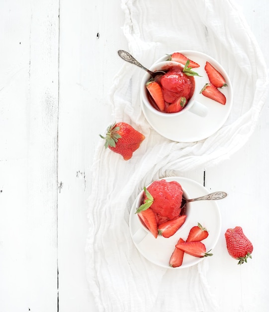 素朴な白い木製の背景の上面図上のカップにミントの葉とイチゴのシャーベットアイスクリーム