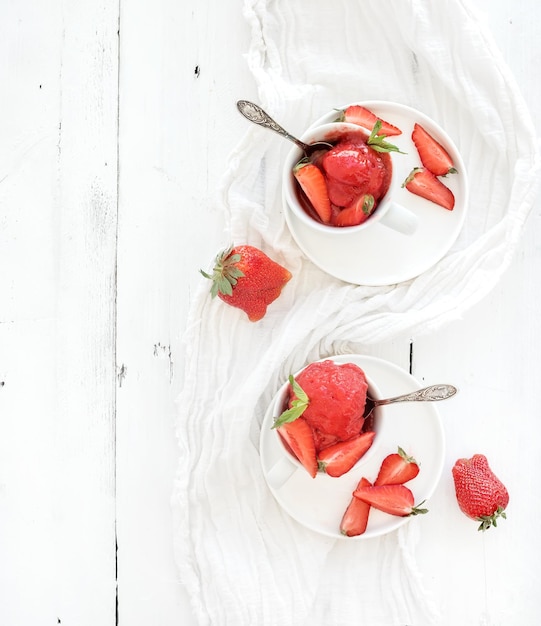 Strawberry sorbet icecream with mint leaves in cups over rustic white wooden background top view