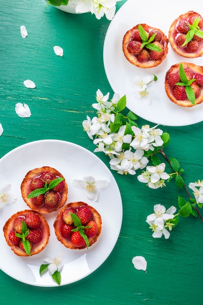 Strawberry tartlet on white plates on green surface, 