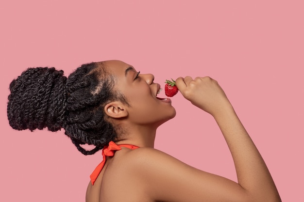 Strawberry tatste. Dark-skinned woman eating strawberries and looking enjoyed