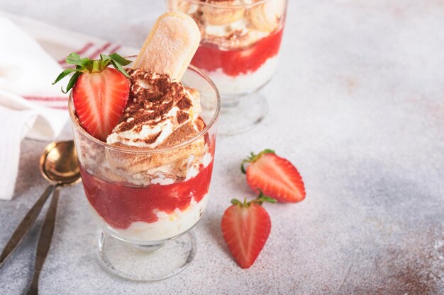 Strawberry tiramisu Traditional Italian dessert tiramisu in glass with fresh strawberry and mint leaves on old gray concrete background table background Copy space Food background