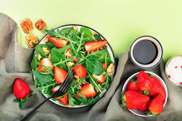 Strawberry Vegan Salad with spinach arugula walnuts balsamic vinegar and olive oil dressing on lime green background Healthy food Top view