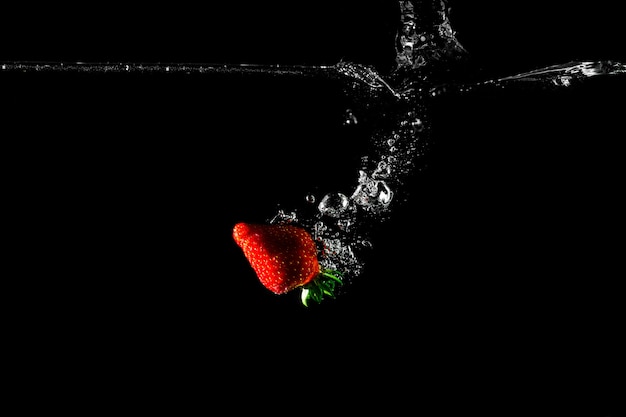 Fragola in acqua con sfondo nero.