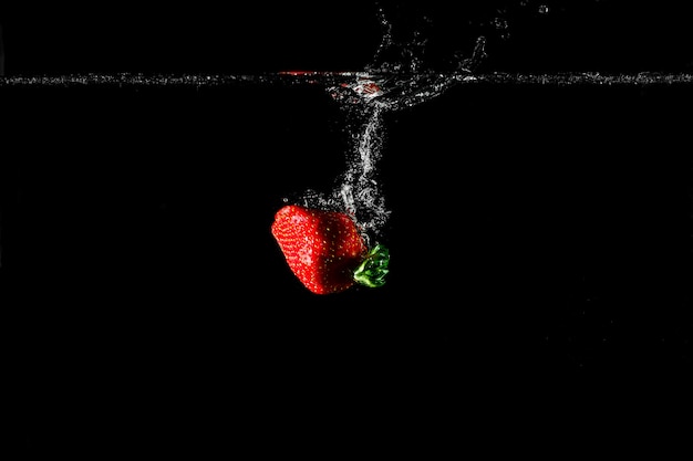 Strawberry in water with black background.